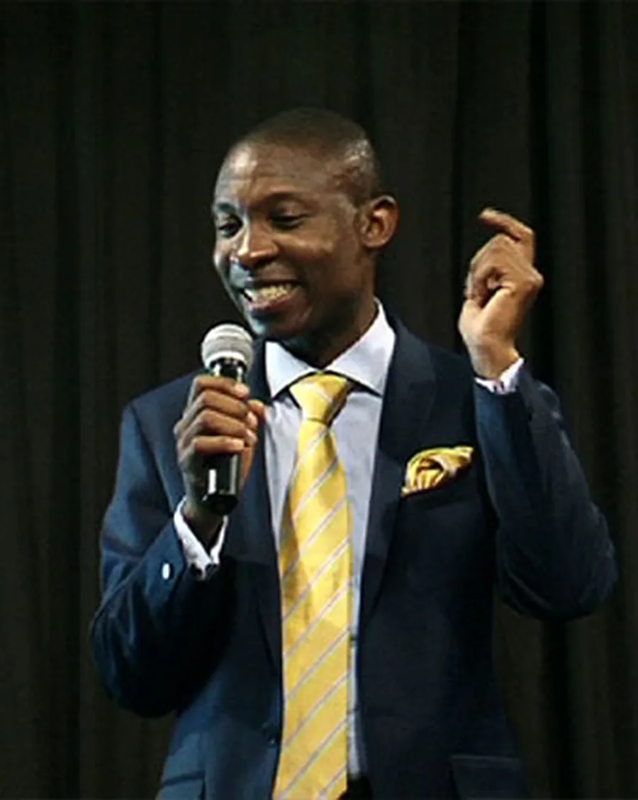 Motivational speaker in a navy suit and gold tie speaking into a microphone